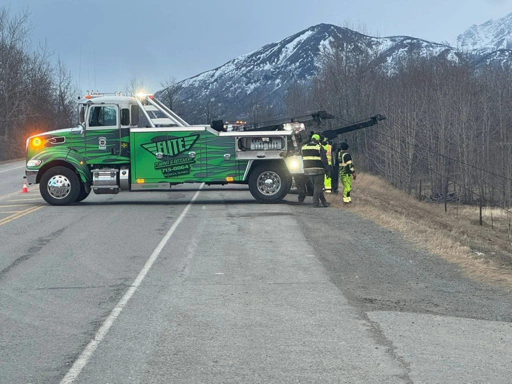 Real Elite Towing green wrecker truck on highway shoulder winching